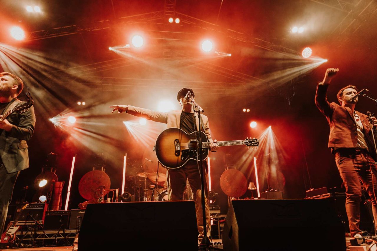 Folk band stood on big stage backlit with red light