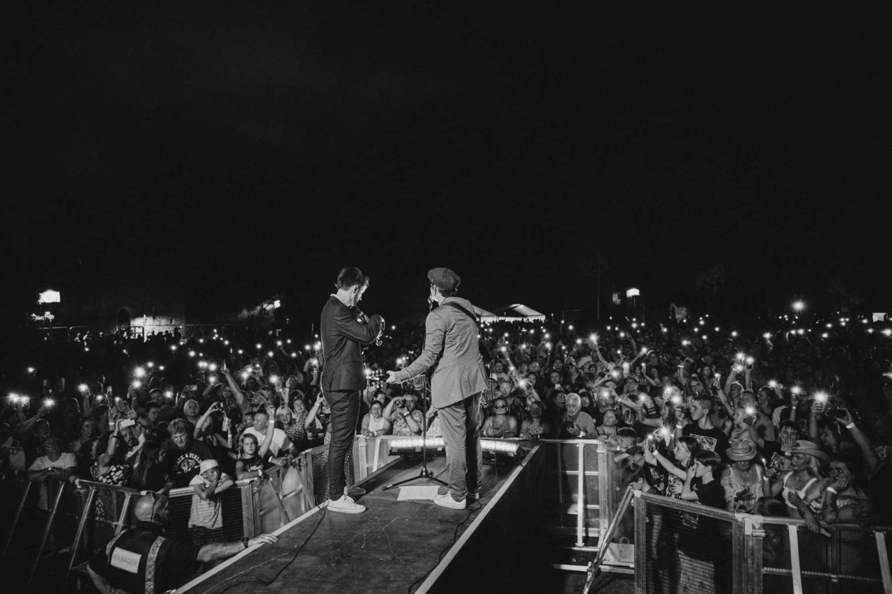 Band stood in front of huge crowd with hundreds of phone lights in the dark