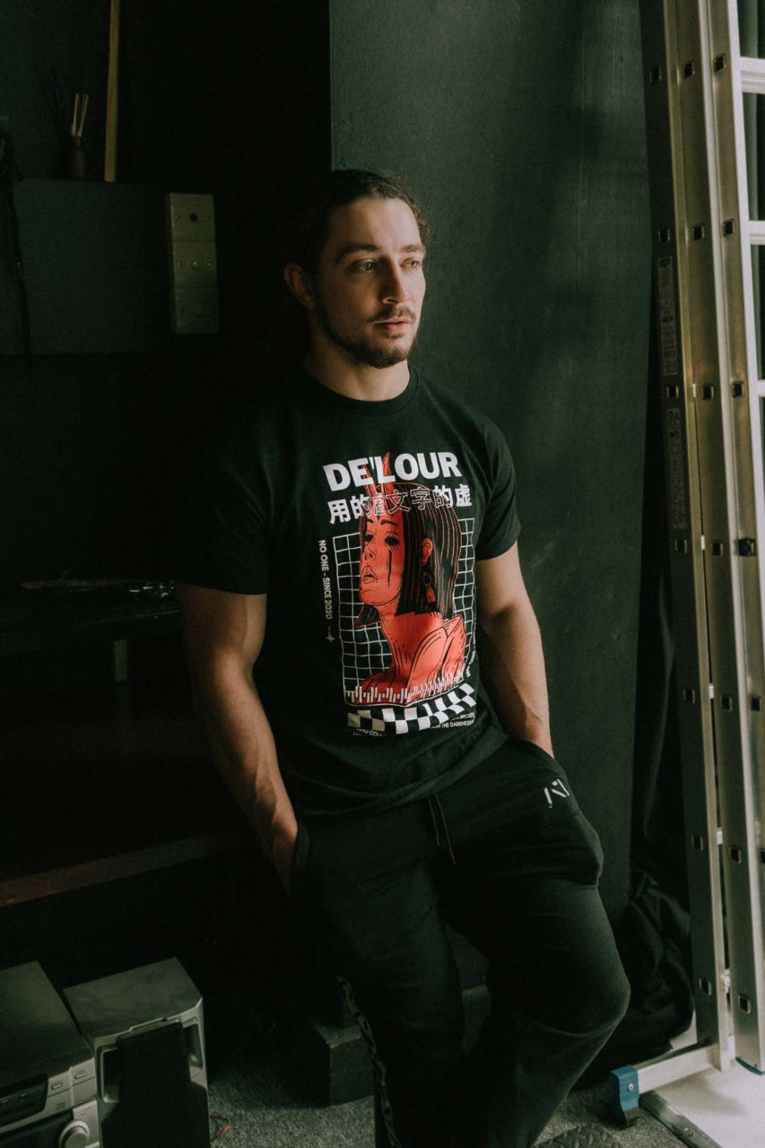 Male model posing in a dark set wearing a black t-shirt