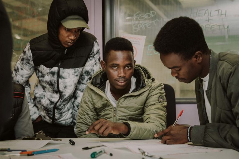 Three young male refugess sat around a table learning to read a map