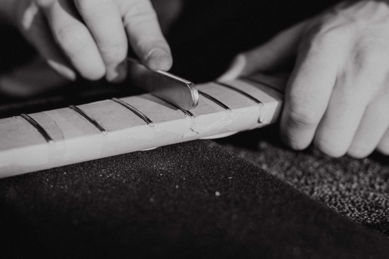 Black and white close up of hands filing a guitar neck