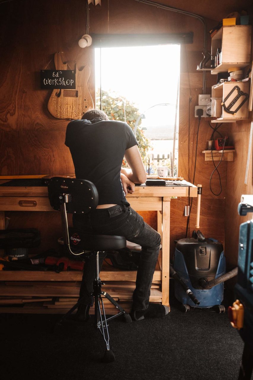 Rear view of a man sat at a window in his workshop with summer light flooding in