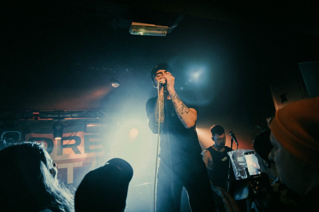 Adam from Glass Heart on stage holding a microphone with both hands while surrounded by the crowd