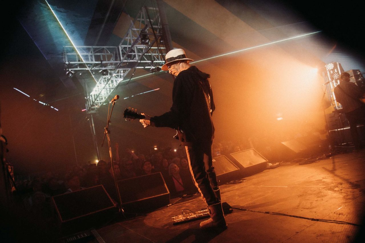 View from behind Dave Brock on stage looking out over the crowd while he plays guitar