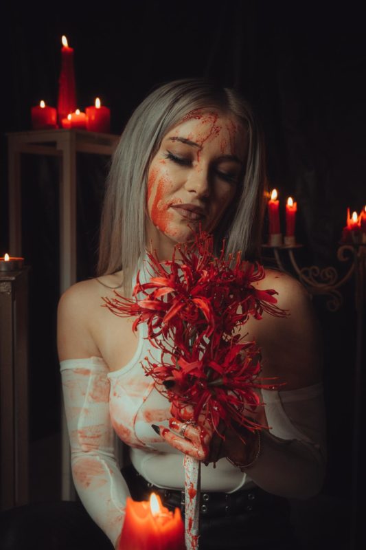 Girl sat in dark lit room surrounded by candles and dripping with fake blood as she worships a scarlet flower