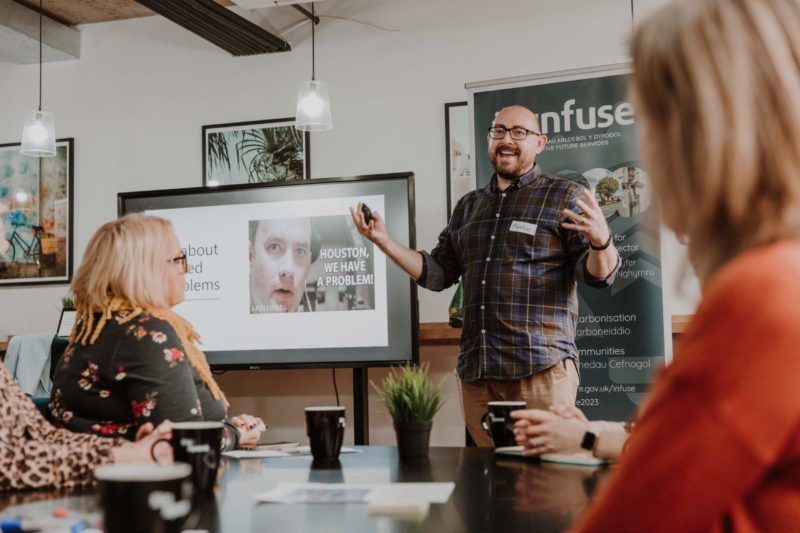 Man stood giving an enthusiastic presentation in a well lit room in Cardiff