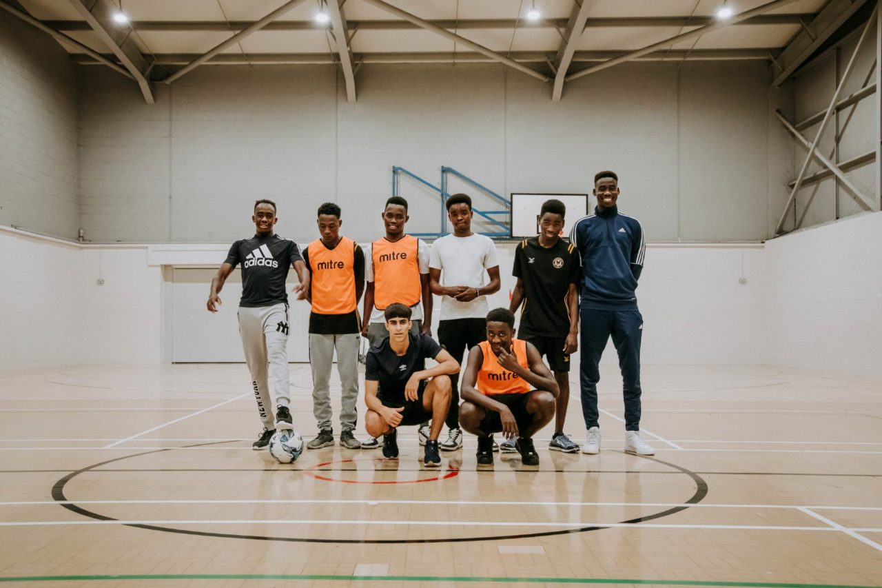 Group of young Eastern refugees stood smiling together in a sports hall as a team