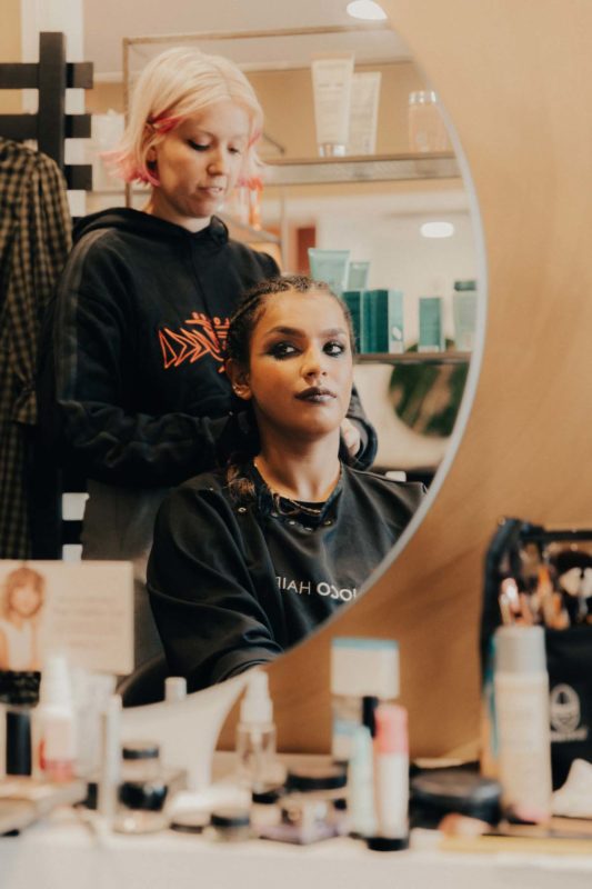 Reflection of Hannah and Sophie in a mirror, surrounded by cosmetics and hair products