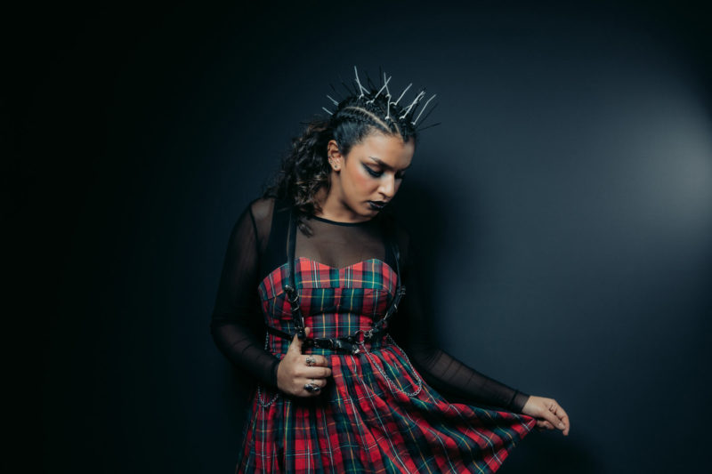 Model in alternative makeup and punk style hairstyle stood against a dark background posing in studio shoot