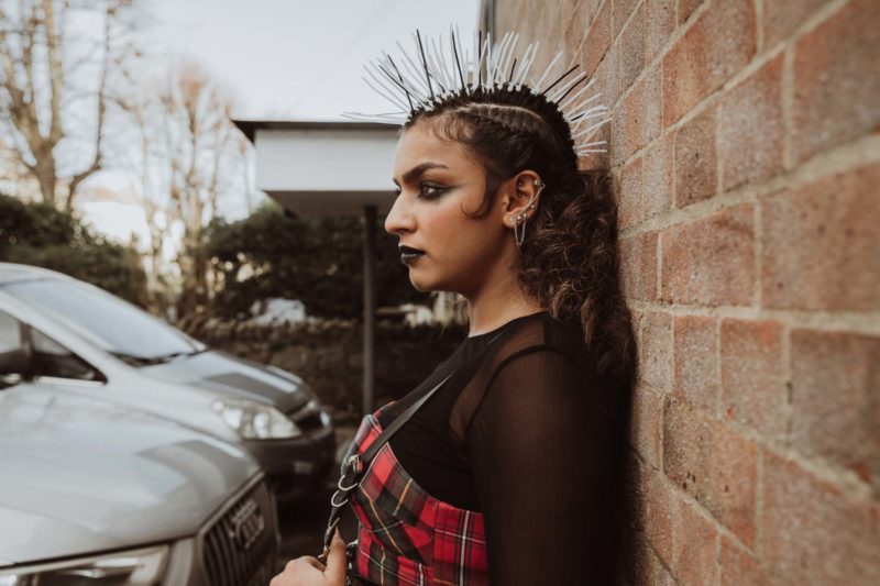 Female punk model with eccentric hairstyle stood against a brick wall