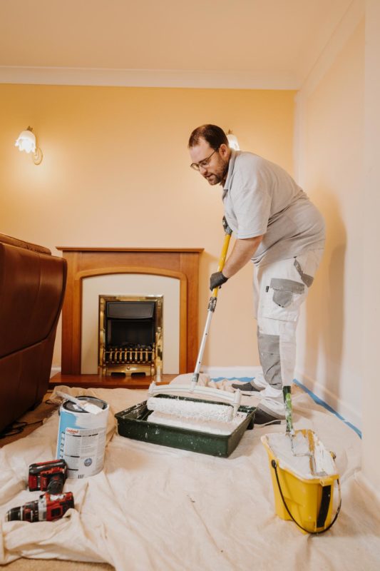 Decorator stood up loaqding up a big roller with paint surrounded by tools