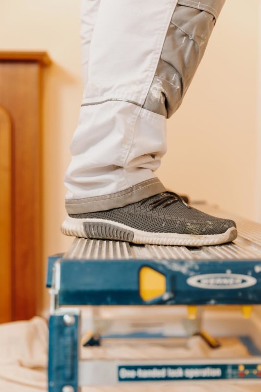 Decorator's feet stood on a dirty blue work ladder