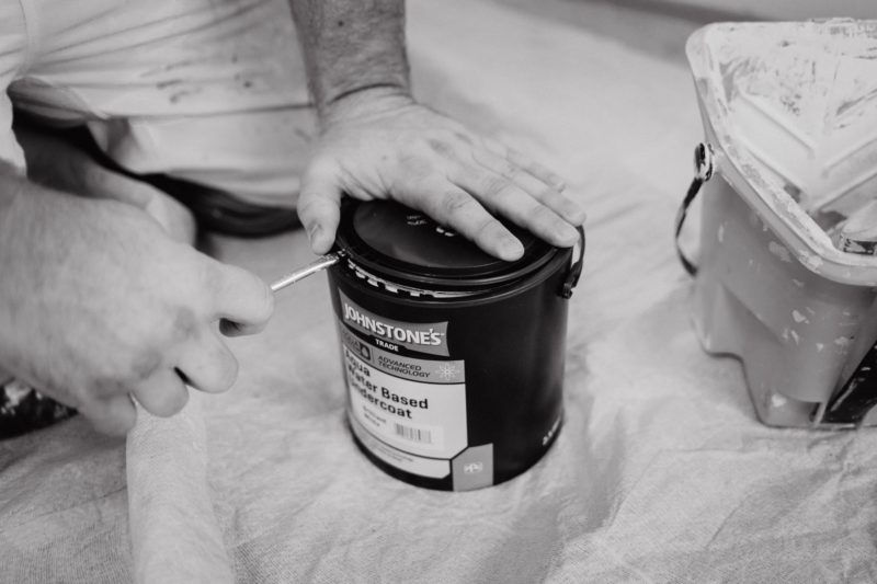 Black and white close up of hands opening a tin of Johnstone's paint with screwdriver