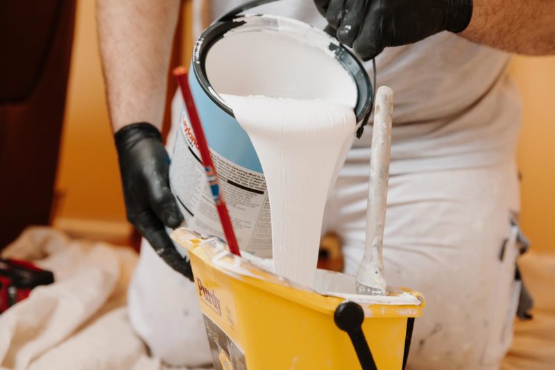 Close up of hands poruing white paint into a yellow bucket