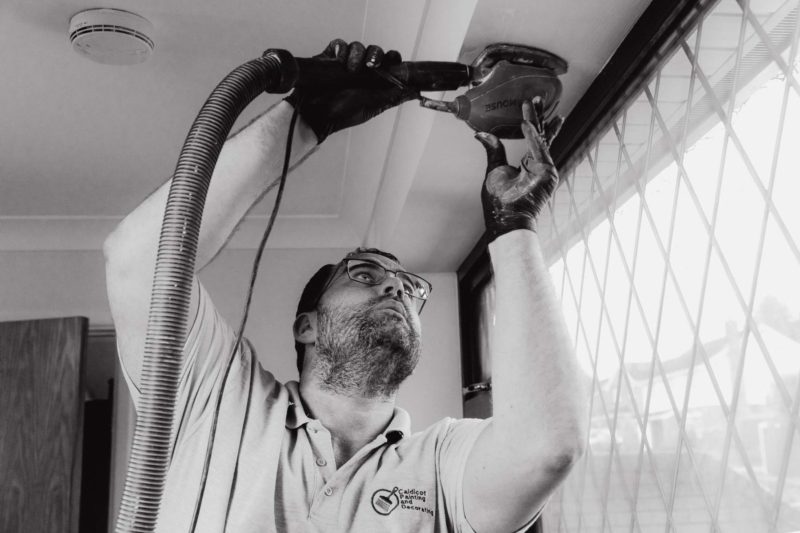 Black and white shot of decorator using an electric sander above his head