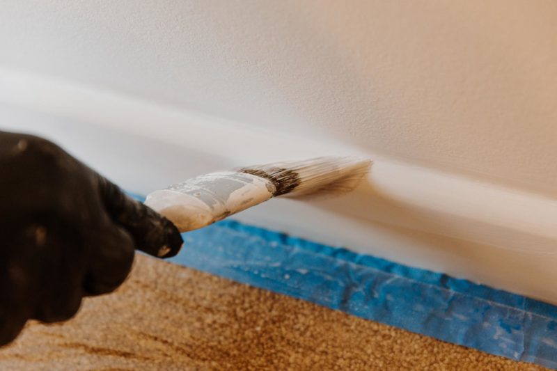 Paint brush running along skirting board with blue tape underneath