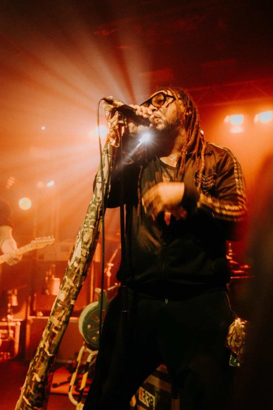 Benji Webbe singing on stage bathed in orange light