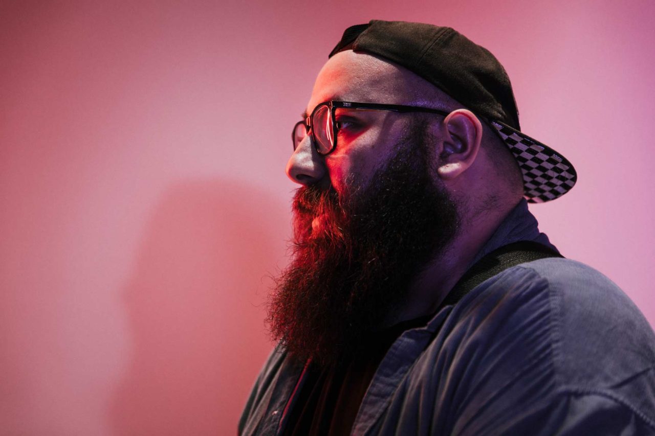 Side profile of man with red light reflected in glasses and pink light in the background