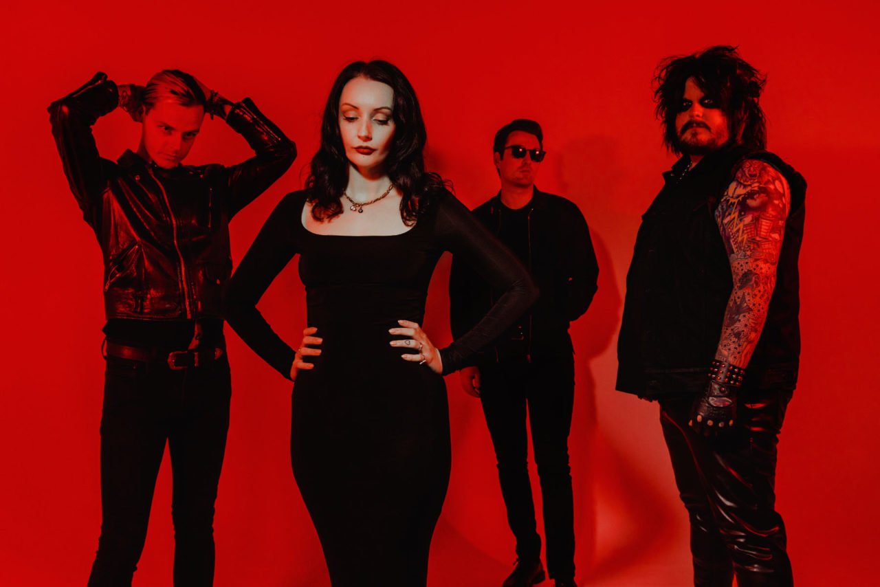 Goth rock band The Nightmares stood in a red lit studio all dressed in black