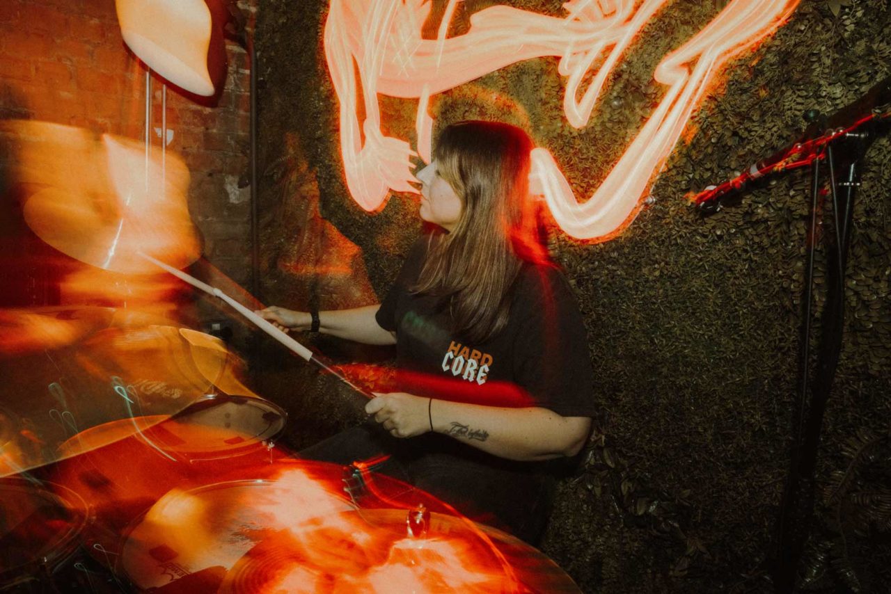 Female drummer from Failstate sat bhind the drum kit with lots of blurry light leaks