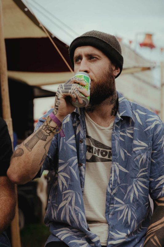 Portriat of a hipster looking man sat drinking a can of Hive Mind mead at Green Gathering Festival 2023
