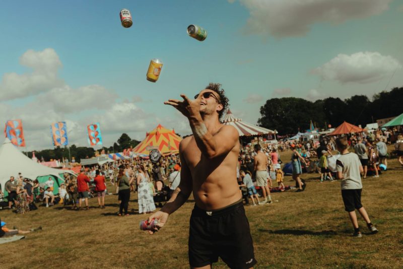 Man at summer festival juggling four cans of mead on a sunny blue day