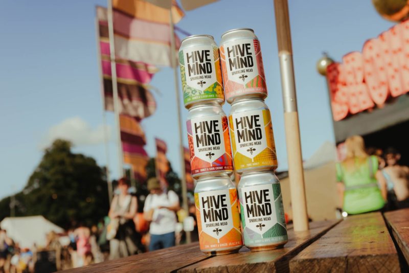 A tower of six colourful cans stood on a table with som eblurry festival flags in the background