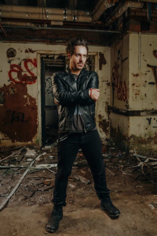 Male rock singer stood in a derelict building surrounded by debris staring off camera