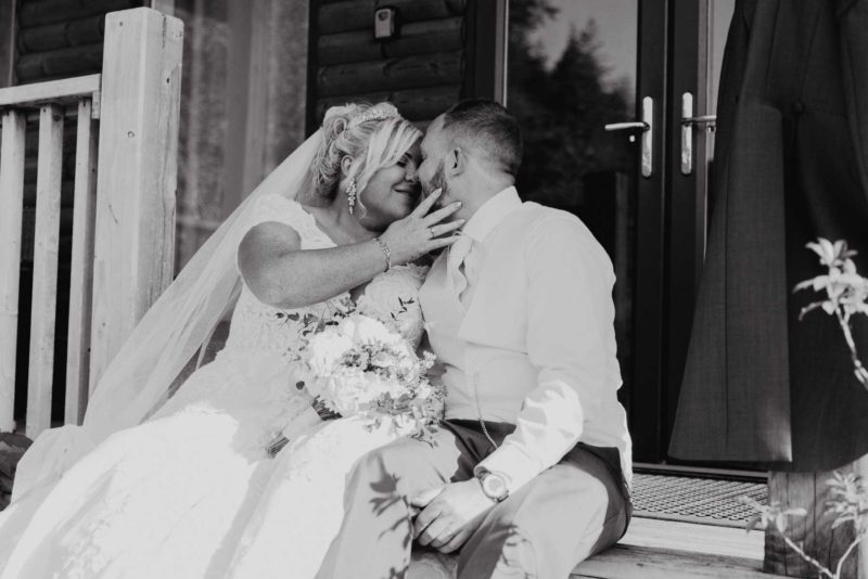 Couple sat kissing on the steps of a lodge