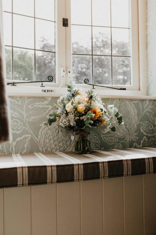 A summery bridal bouquet sat in a rustic window bathed in morning light