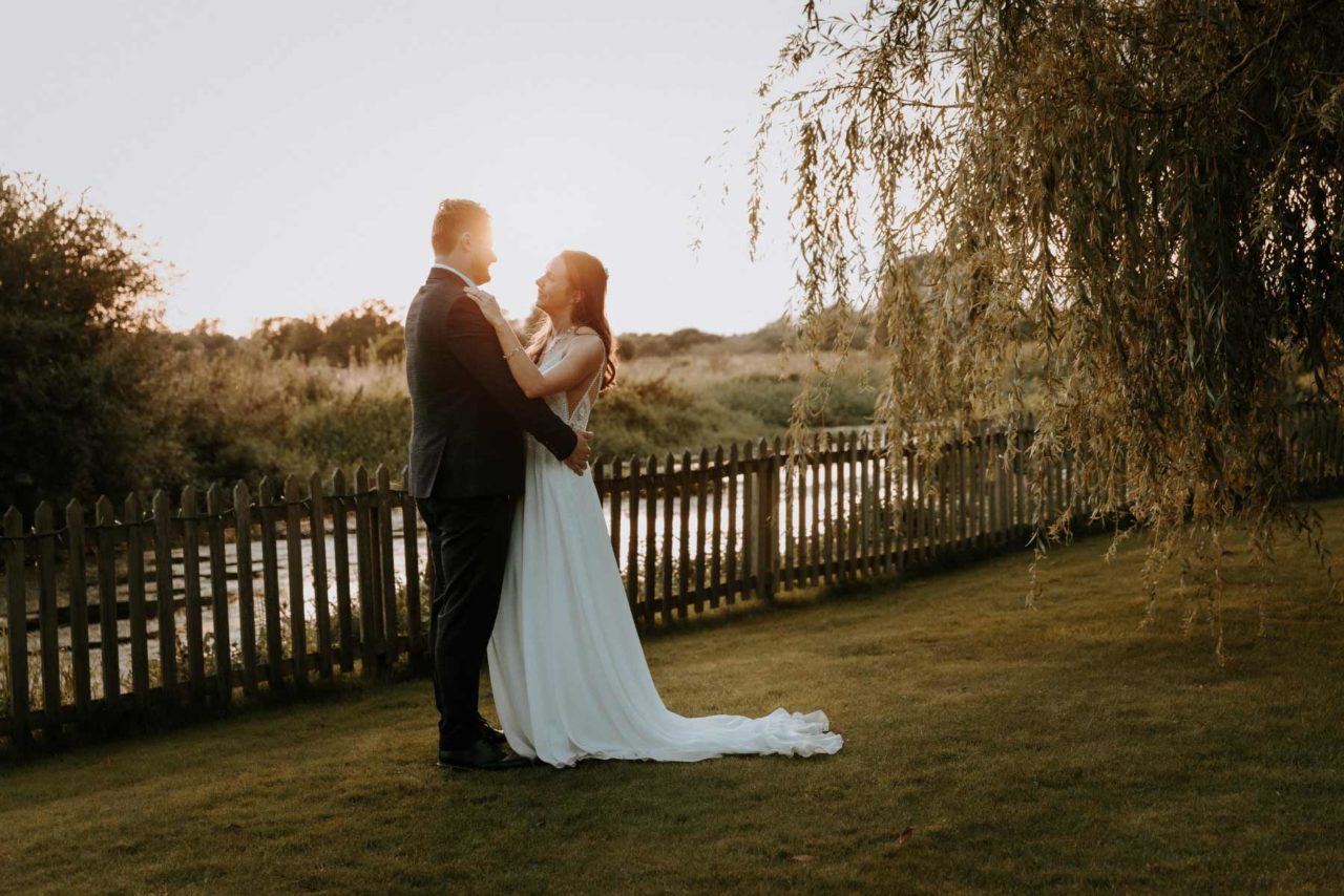Husband and wife stood happily against a sunset at a beautiful summer wedding
