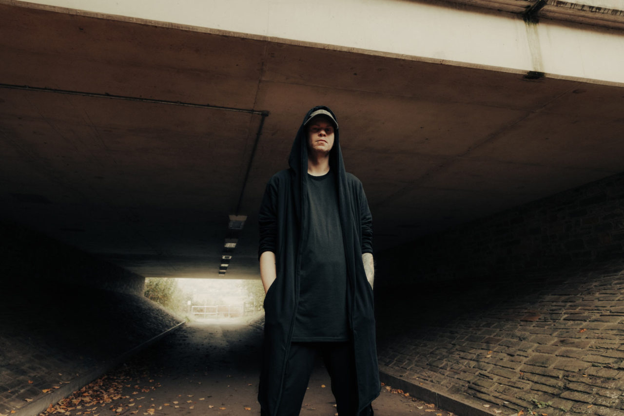 Rapper with face covered in shadow stood beneath an underpass