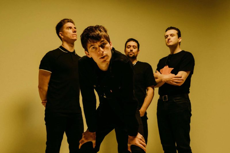 Indie rock band from Newport stood on set with singer leaning into the camera, covered in yellow light