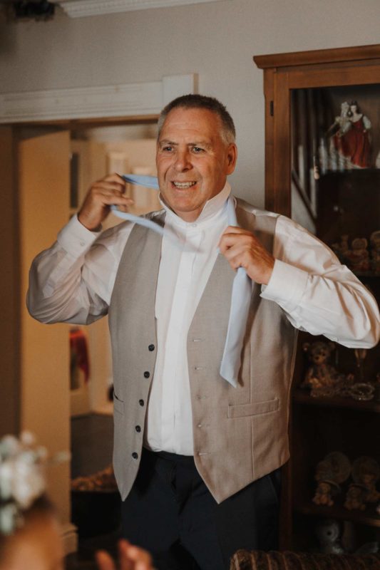 Father of the bride getting dressed and putting on his tie
