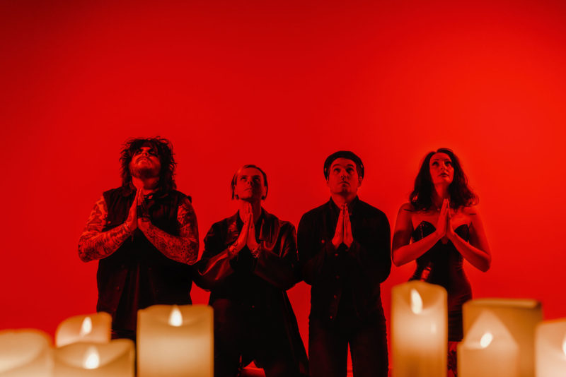 Goth pop band knelt praying in a red-lit studio with candles in the foreground. Shot in Digichemistry studio in 2023.