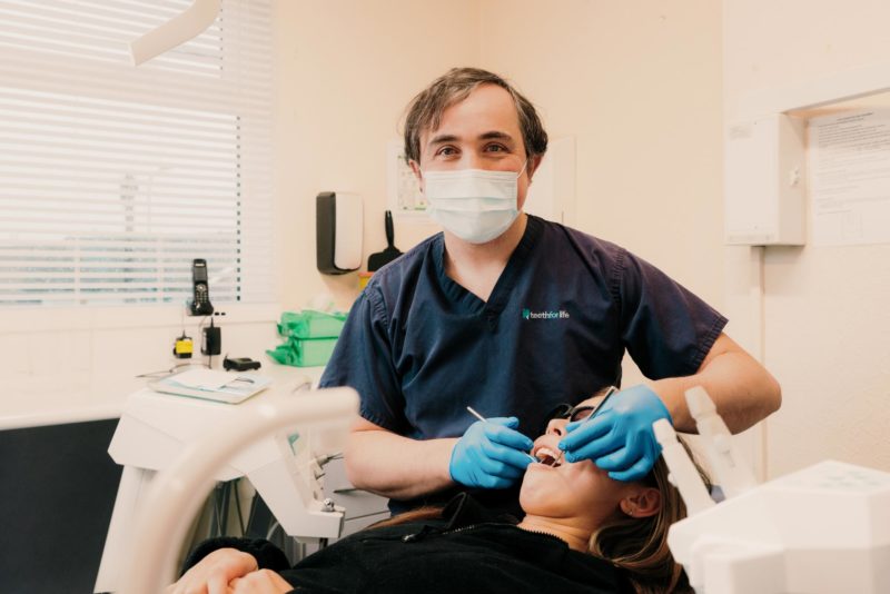 Dentist smiling towards the camera while examining a patient. Shot for a commercial portrait shoot for Teeth For Life.