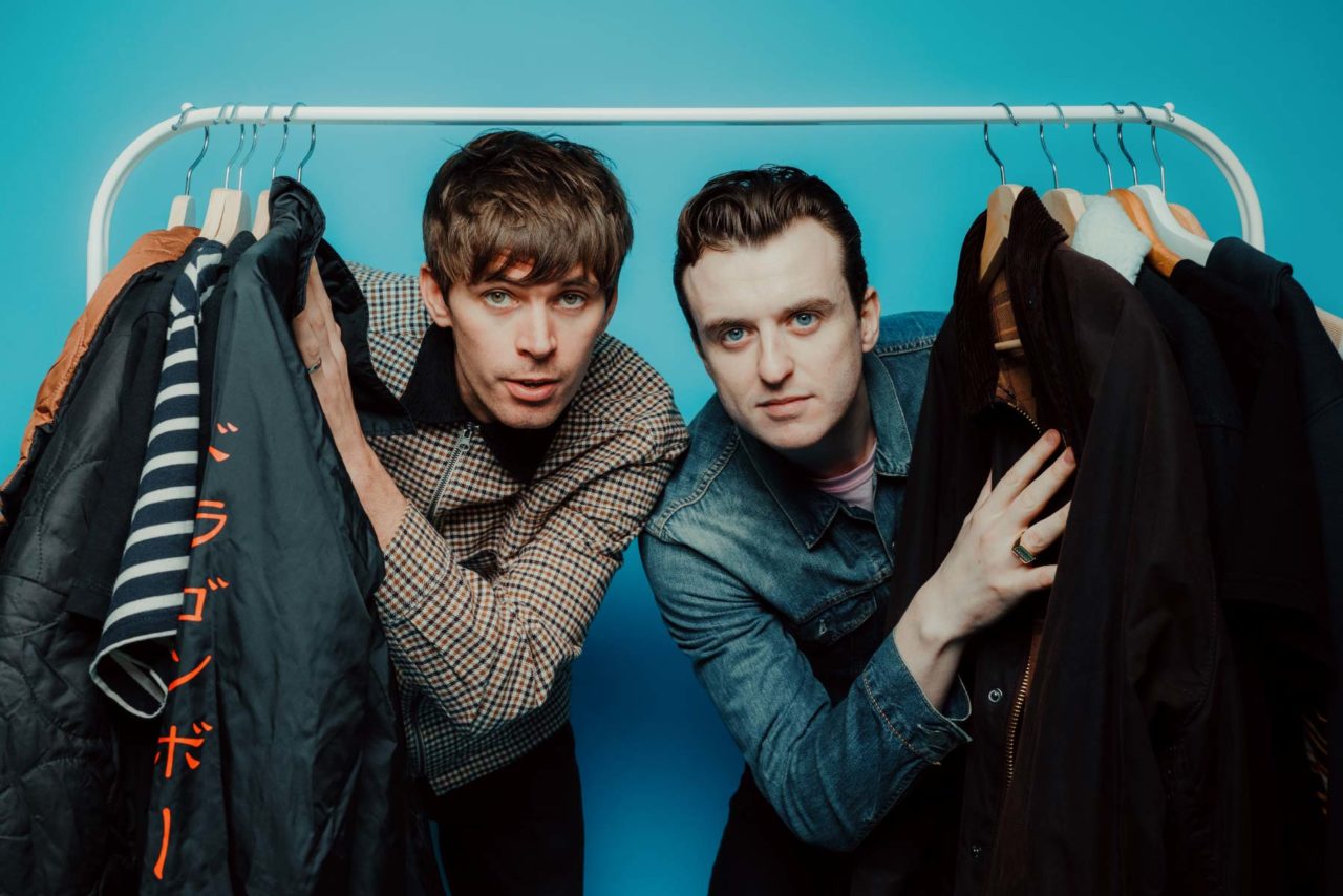 Two men stood rummaging through a clothes rack in front of a bright blue backdrop during a promotional shoot. Shot at Citrus Studio Cardiff.