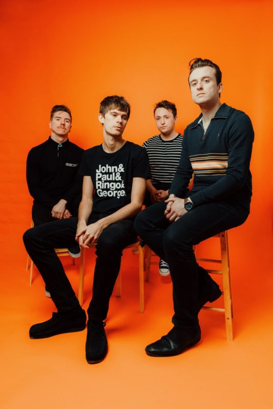Newport Indie band Eurekas sat on stools in front of an orange backdrop at Citrus Studio, Cardiff.