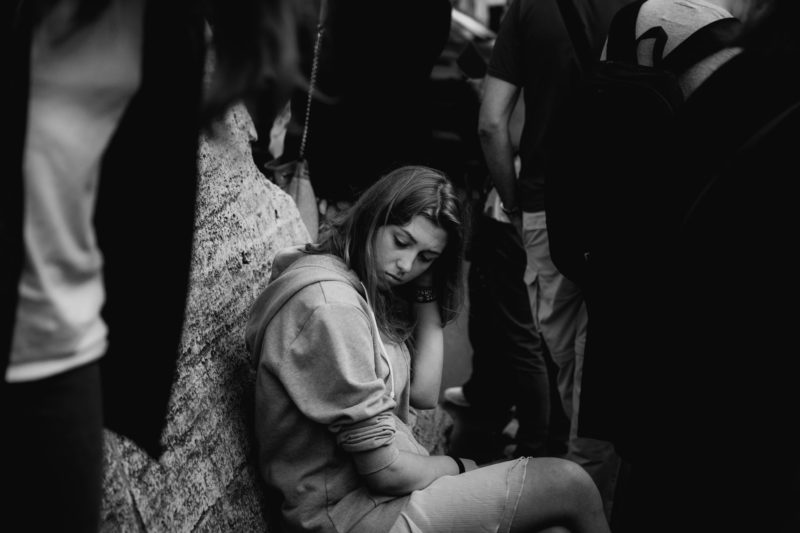Personal work. Black and white shot of a sad looking teenage girl sat in a queue outside Vatican City, surrounded by adults.