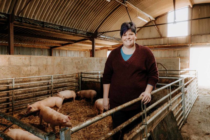 Marketing portrait of Monmouthshire Fayre, Jessi, stood smiling in a pig pen on her Portskewett Farm.