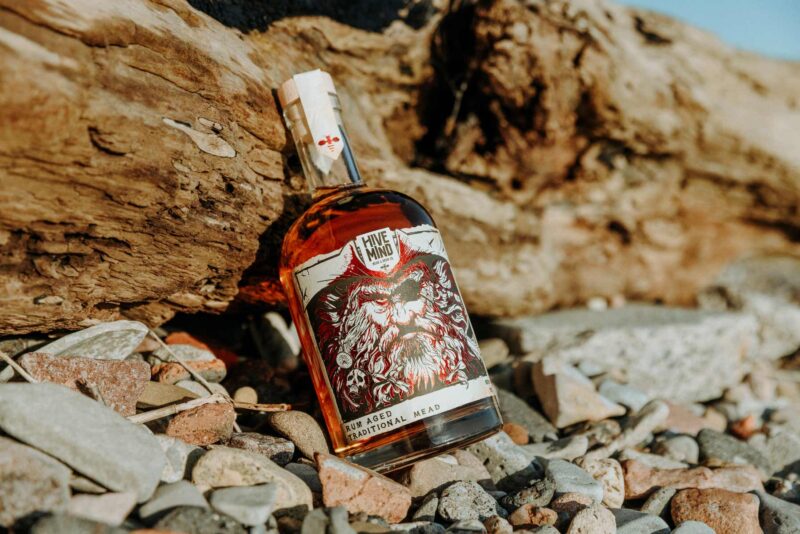 Promotional product image of a bottle of Hive Mind rum aged mead set in a coastal, shipwrecked styled setting. Shot as part of a promotional marketing</p/> <a href=